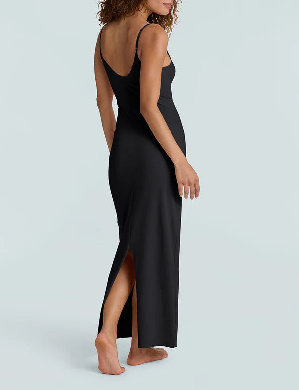 Woman wearing a black slip dress with a high slit on a light gray background