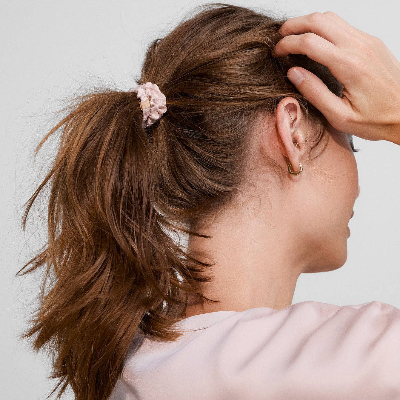 Woman with a ponytail wearing earrings against a neutral background