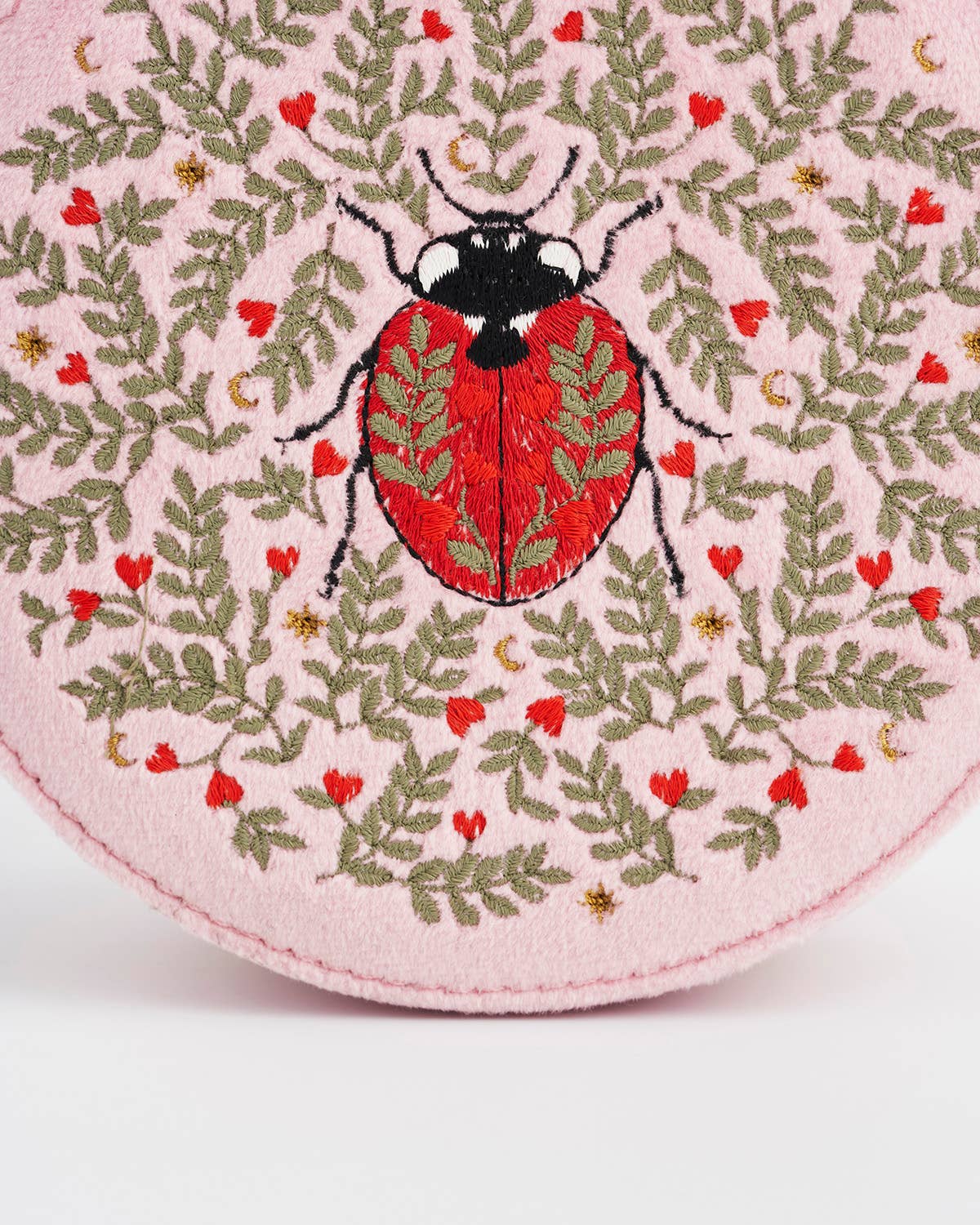 Embroidered ladybug design on a pink fabric background with green leaves and red flowers.