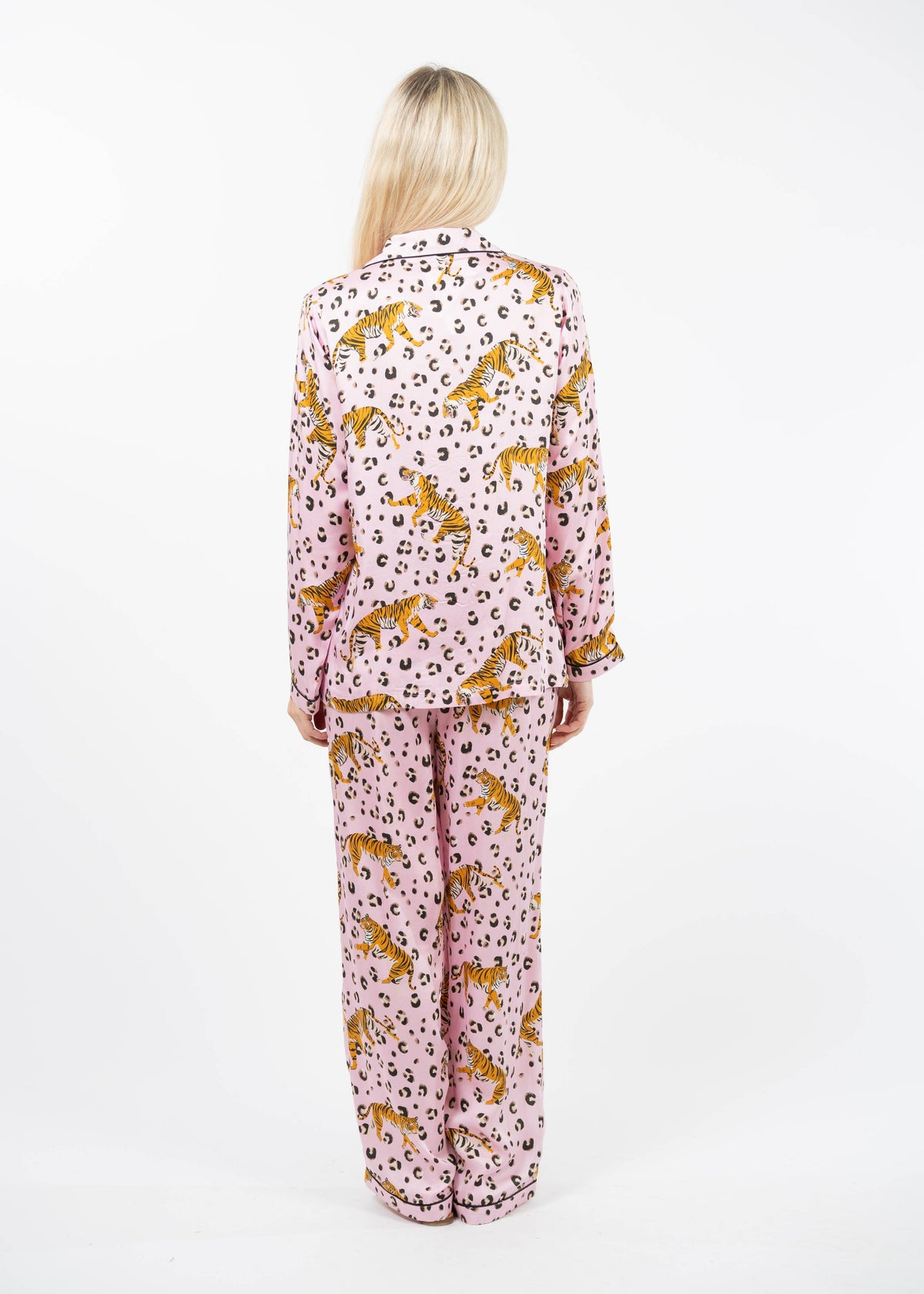 A woman viewed from behind wearing a matching pajama set with a pink base, leopard print, and orange cheetah motifs, photographed against a plain white studio background.