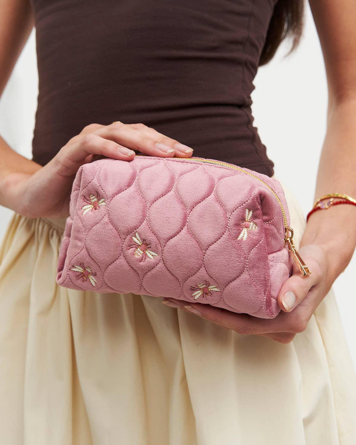 Person holding a pink quilted clutch with floral embroidery