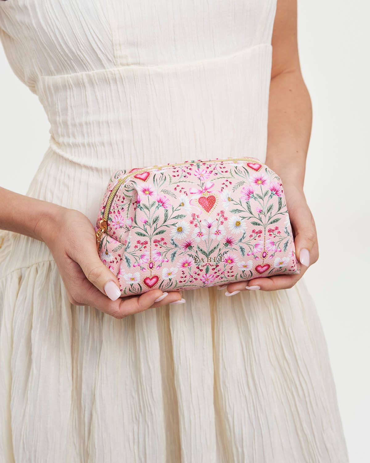 Floral patterned pouch held by a person wearing a white dress.