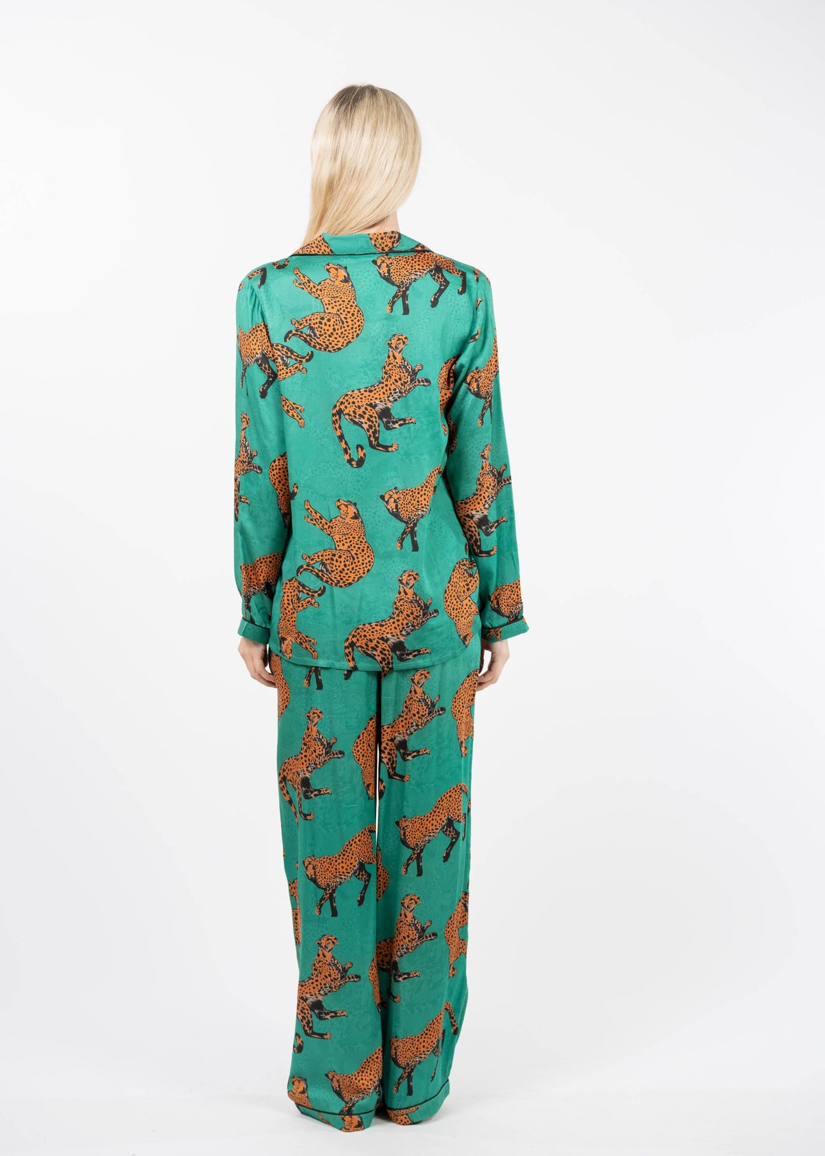 A woman viewed from behind wearing a matching two-piece pajama set in teal green with an orange and black leopard print, set against a plain white studio background.