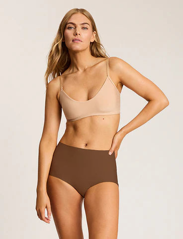 Woman wearing a beige bikini top and brown high-waisted bikini bottom on a plain background