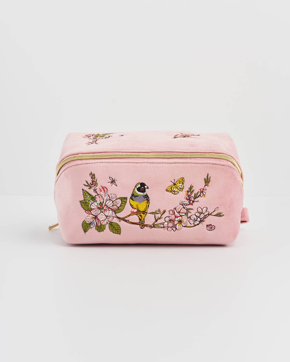 Pink makeup bag with floral and bird embroidery on a light gray background