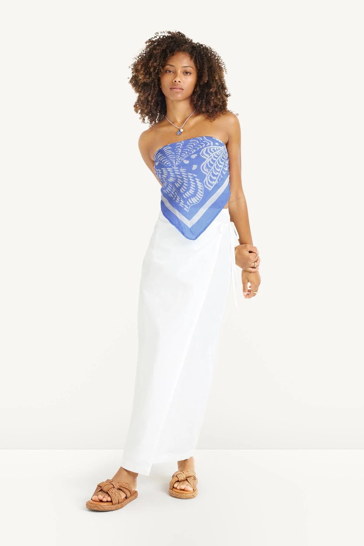 Woman wearing a strapless blue and white patterned top with white pants on a white background