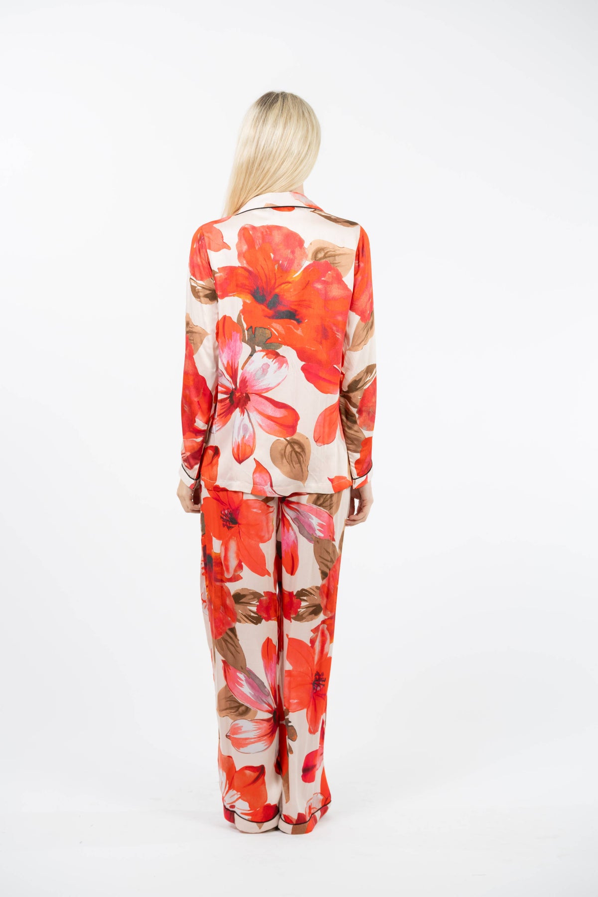 A woman viewed from behind wearing a matching long-sleeve blazer and wide-leg trousers set in a warm beige fabric with a bold red, orange, and pink floral print.