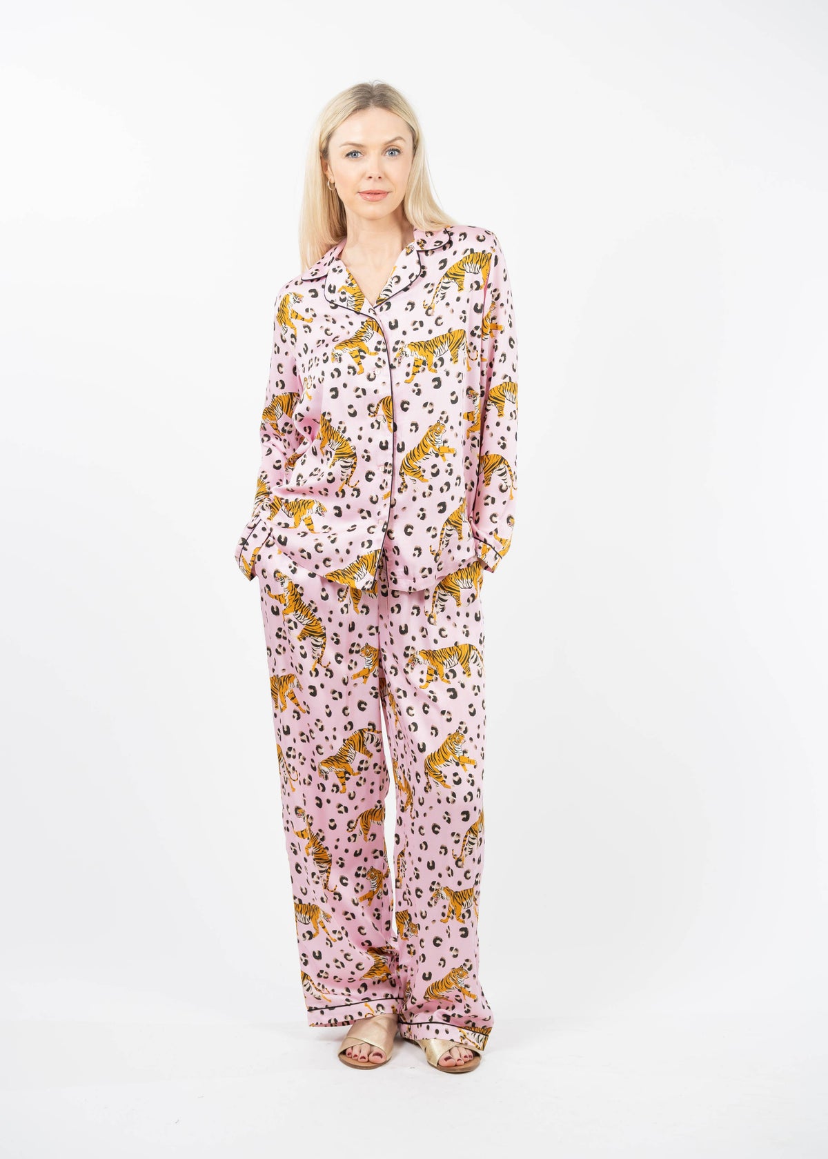 A woman modeling a matching two-piece pajama set with a pink background and a leopard print pattern, standing against a plain white studio background.