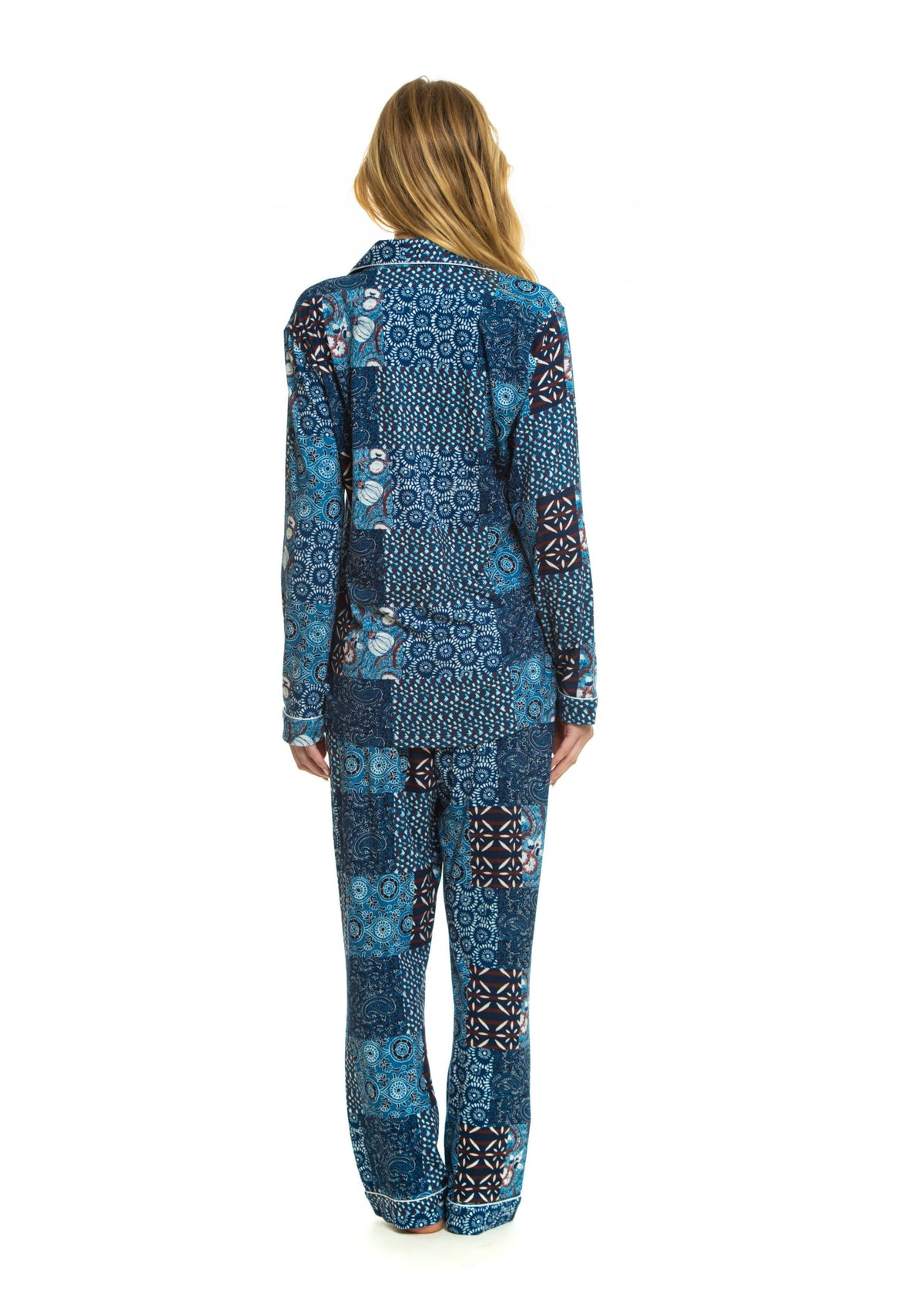 A woman viewed from behind wearing a matching long-sleeve top and pants pajama set with a blue patchwork print featuring various geometric and floral patterns.