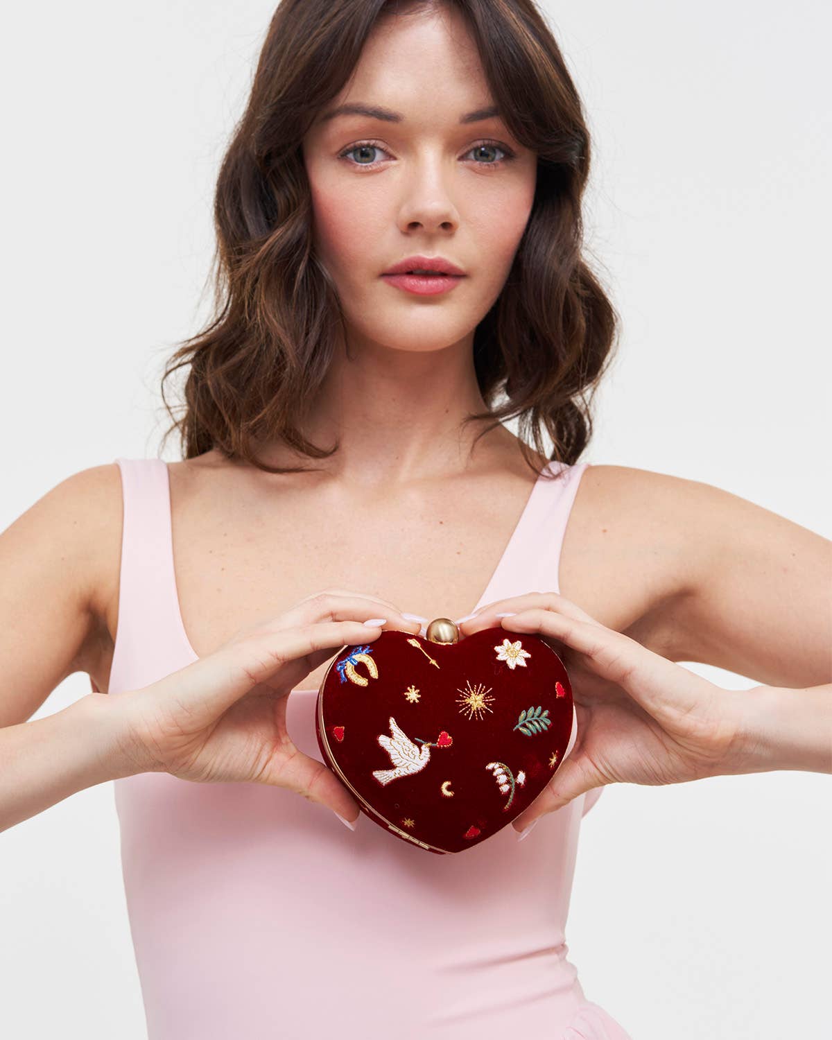 Woman holding a heart-shaped clutch with decorative elements against a plain background