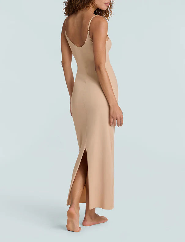 Woman wearing a beige slip dress with a slit on a light gray background