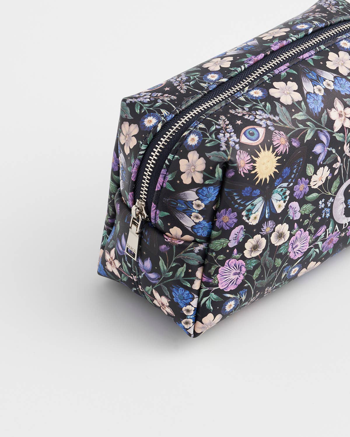 A rectangular zippered pouch with a black background covered in a dense floral and occult-themed print featuring purple, blue, pink, and white flowers, butterflies, and an eye of providence, shown on a light gray studio background.