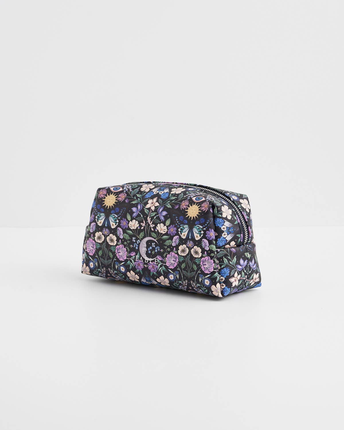A small zippered cosmetic pouch with an all-over floral print in purple, pink, blue, and yellow on a dark background, photographed on a clean white studio background.