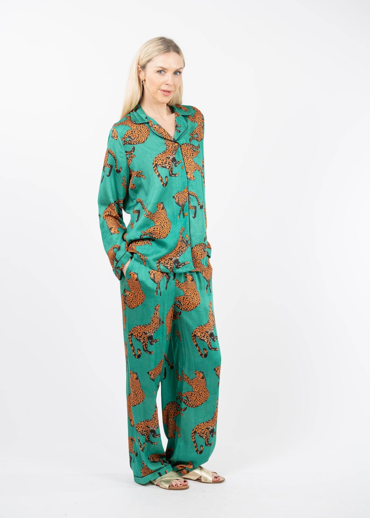 A woman modeling a matching two-piece pajama set with a green base and an orange leopard print, standing against a plain white studio background.