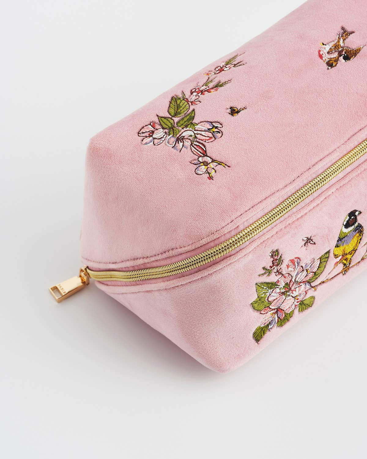 Pink pouch with gold zipper and floral embroidery on a light gray background