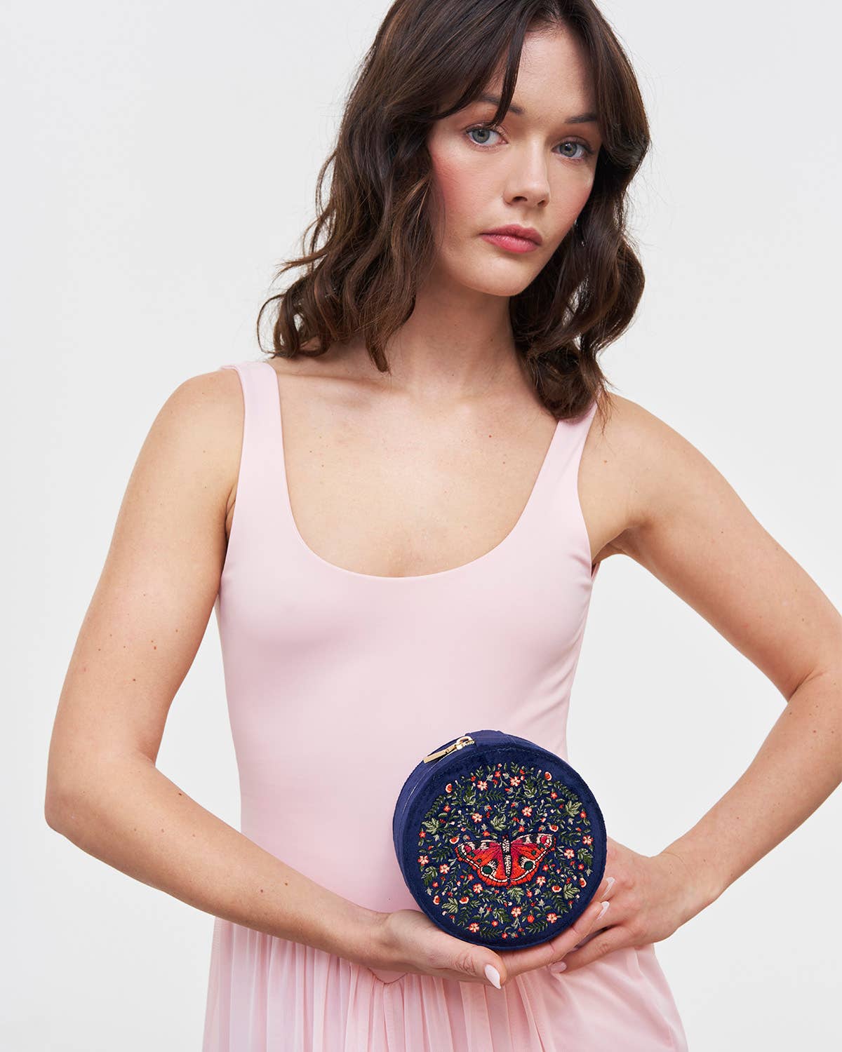 Woman holding a round, floral-patterned clutch bag against a plain background