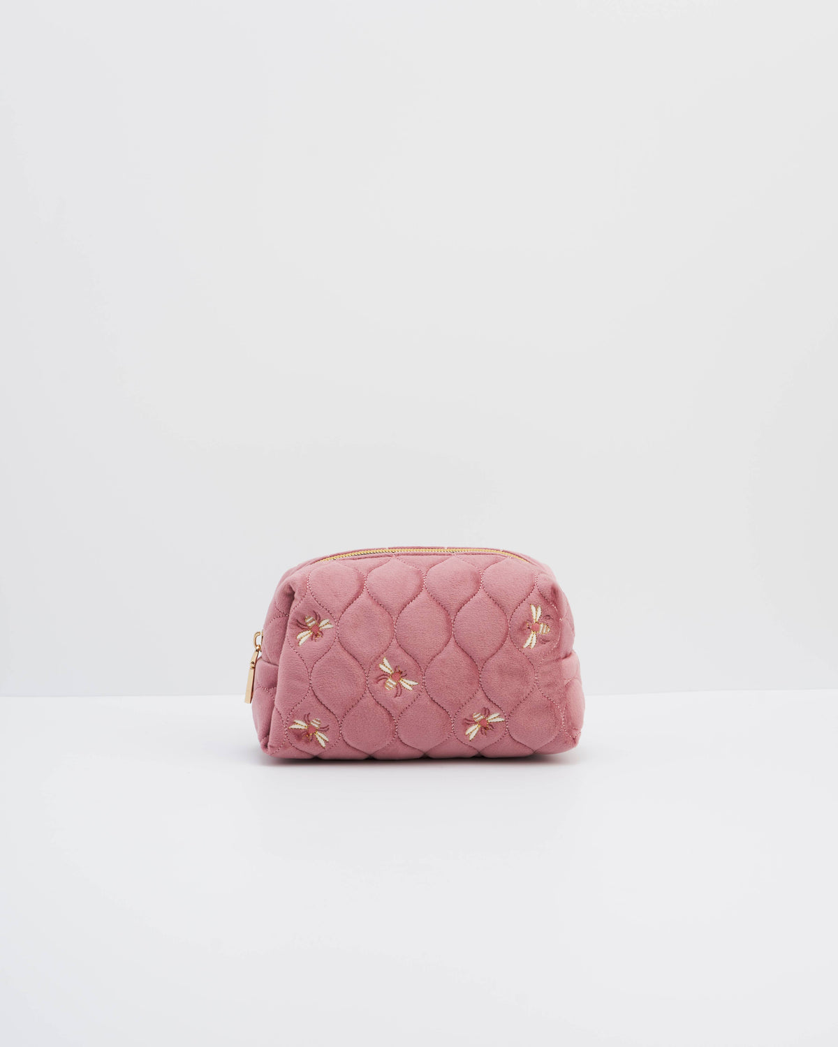 A pink quilted cosmetic pouch with embroidered floral details and gold-tone hardware, photographed on a clean white studio background.