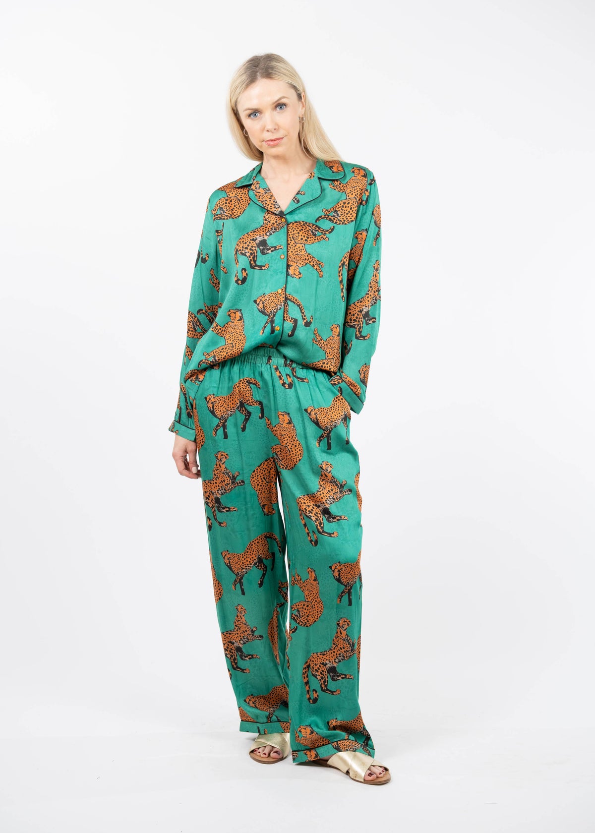 A woman modeling a matching two-piece pajama set with a green base and an all-over brown animal print, photographed against a plain white studio background.
