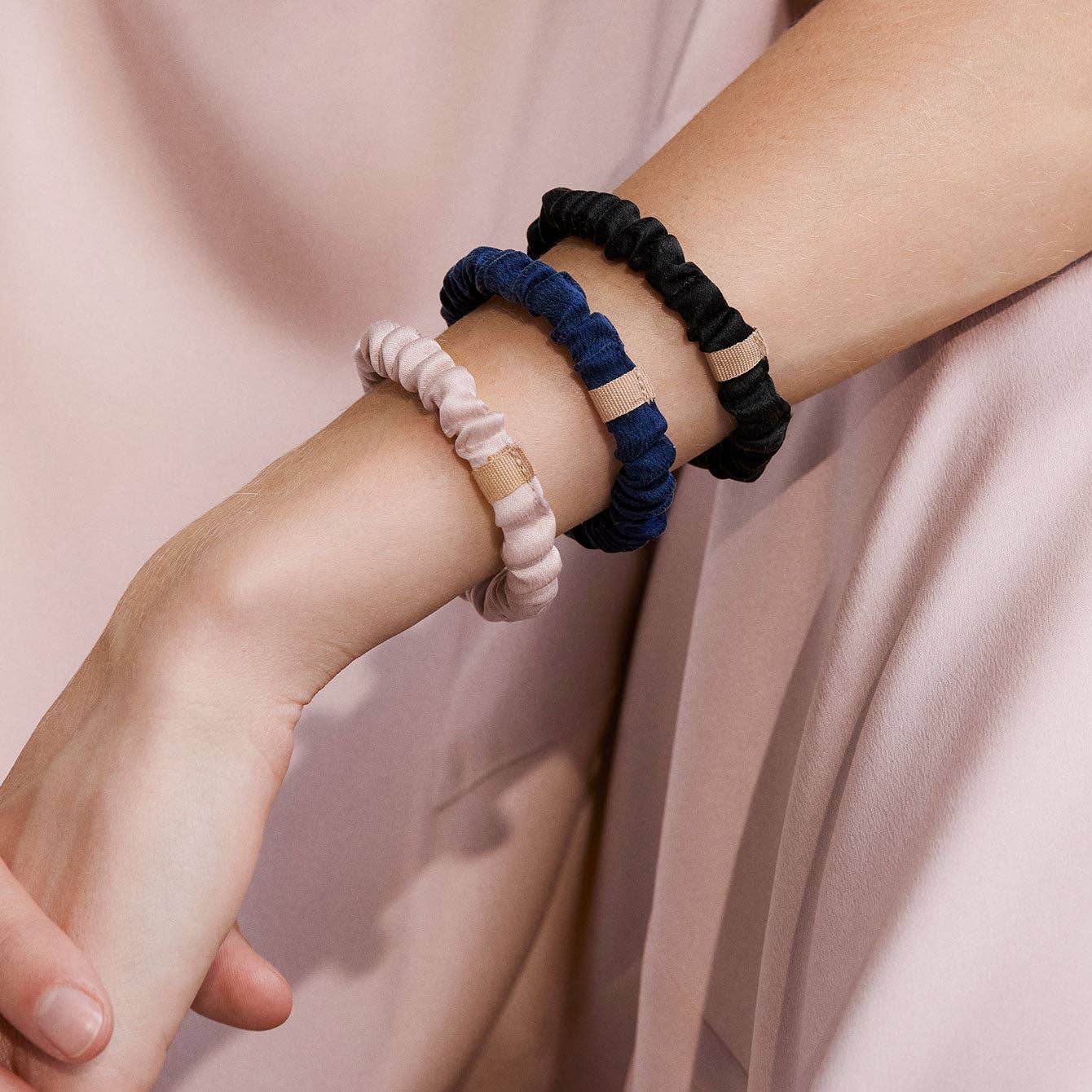 Three hair ties in black, blue, and pink on a wrist against a soft pink background