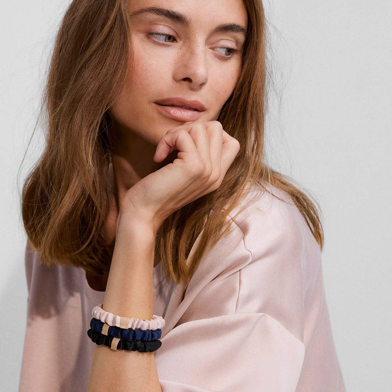 Woman wearing multiple bracelets on her wrist against a plain background