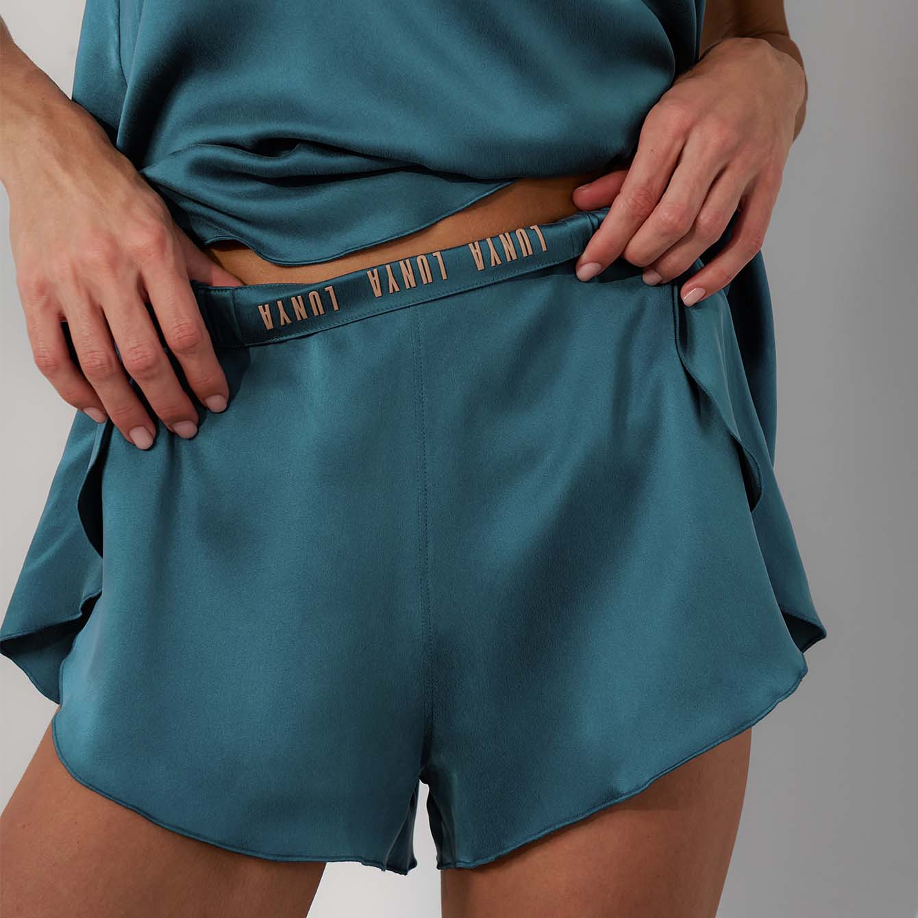 Teal satin shorts with a belt on a gray background